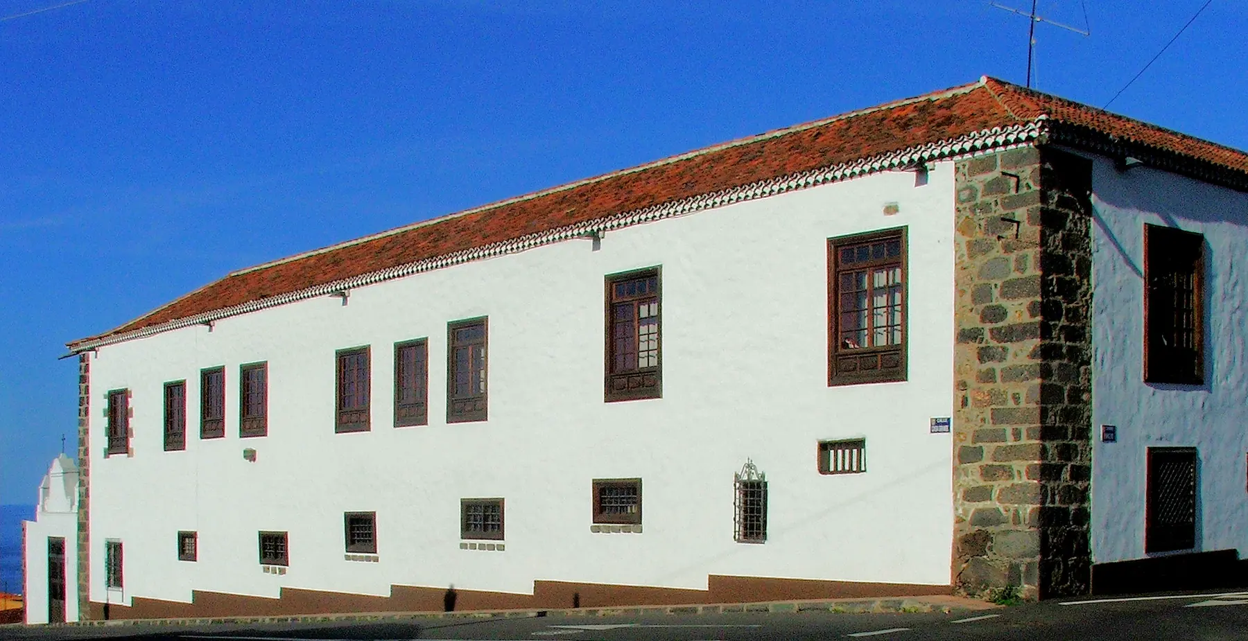 The long whitewashed front of Casa Ábaco under a blue sky, with a red tile roof, dark stone corners and brown wooden windows