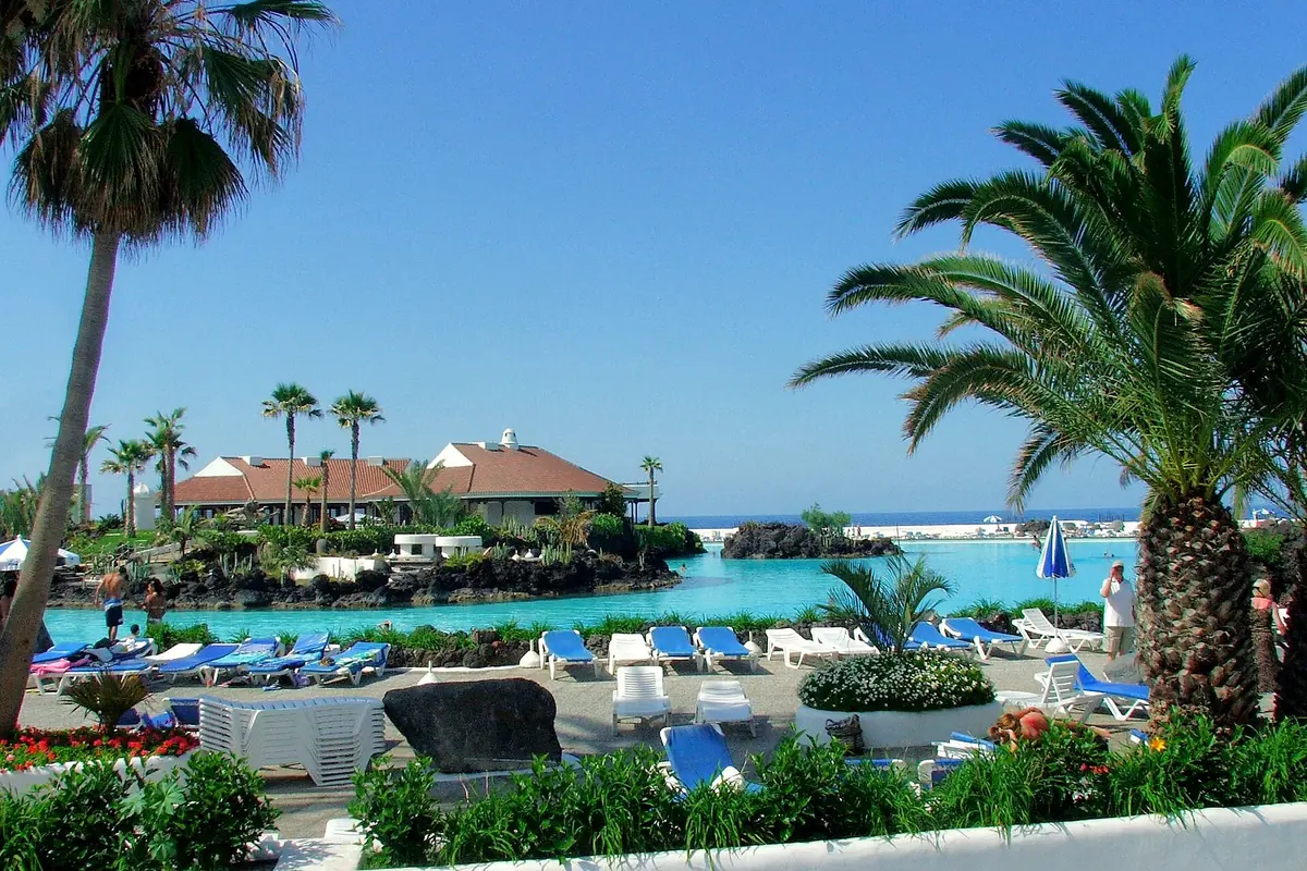 Turquoise seawater pools with sun loungers, palms and low red-roofed buildings at Lago Martiánez under a clear blue sky